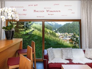 Ein Zimmer mit Blick auf ein Dorf, ein Holztisch, ein rotes Sofa und eine Orchidee im Topf.