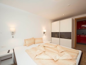 Ein modernes Schlafzimmer mit einem großen Bett, Nachttischen und einem durch eine geöffnete Tür einsehbaren Badezimmer mit rotem Rahmen.