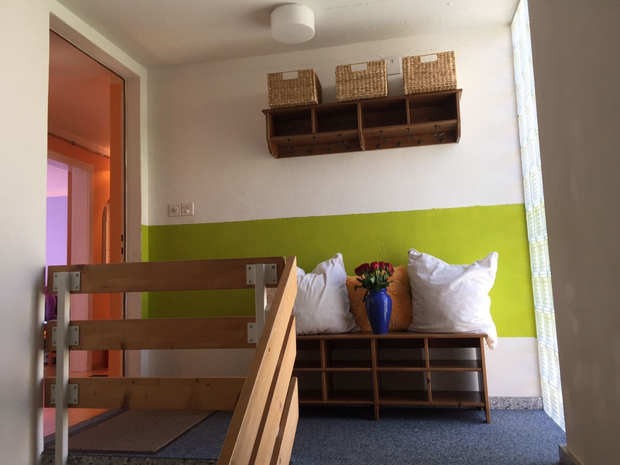 A room with a bench, a wall-mounted shelf with baskets, and a door leading to another room.