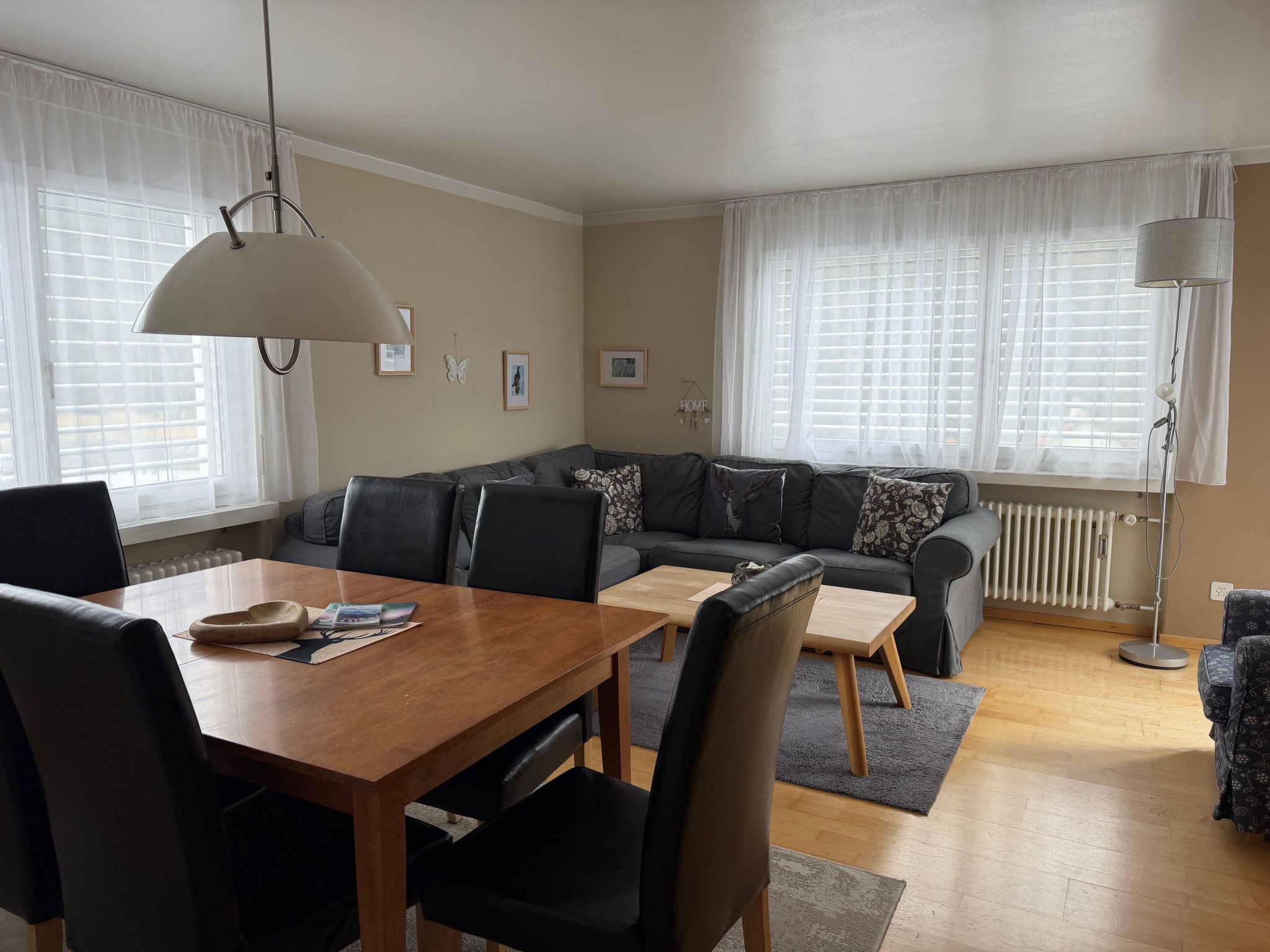 A modern living room with a wooden dining table, black leather sofa, and a grey floor.
