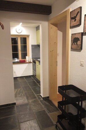 Un corridoio stretto che conduce a una cucina con una finestra, una porta e una passeggino nero per neonati.