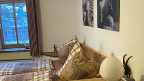 Un dormitorio con dos camas, un aparador de madera, un ventanal con cortinas y cuadros colgados en la pared.