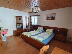 A bedroom with a wooden ceiling, a bed with striped bedding, a bedside table, a mirror, a window with curtains, and a painting on the wall. - Ferienhaus Plaun Grond, (Tschierv) by Interhome (Tschierv)
