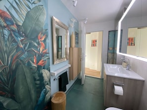 A bathroom with a large mirror, a sink, a toilet, and a wall with a tropical mural. - Chasa Uleiva, (Samnaun-Compatsch) by Interhome (Samnaun)