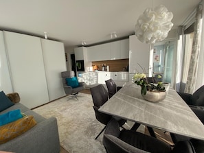 A modern living room with a dining area, a kitchen in the background, and a large white flower chandelier. - Chasa Uleiva, (Samnaun-Compatsch) by Interhome (Samnaun)