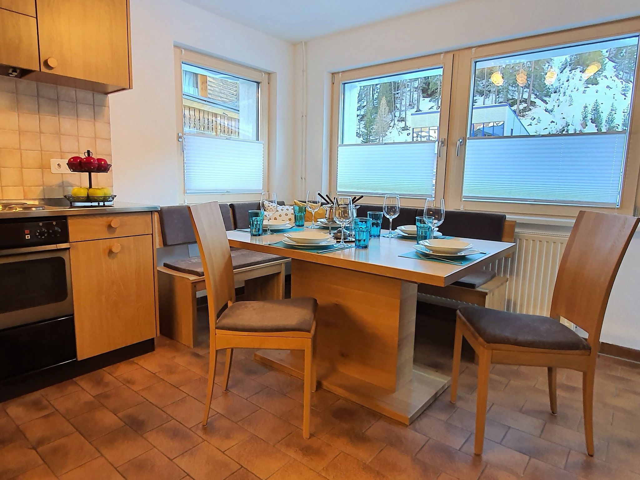 A kitchen with a dining table, chairs, a stove, and a window with a view of trees.