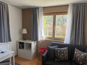 A room with a sofa, a small table, a lamp, a bookshelf, and a window with curtains. - Chasa Bazzi, (Scuol) by Interhome (Scuol)