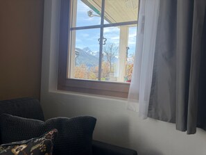 A room with a window overlooking a mountainous landscape, a sofa with patterned cushions, and sheer curtains. - Chasa Bazzi, (Scuol) by Interhome (Scuol)