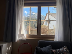 A room with a window overlooking a mountain landscape, a red chair, and a sofa with a floral pillow. - Chasa Bazzi, (Scuol) by Interhome (Scuol)