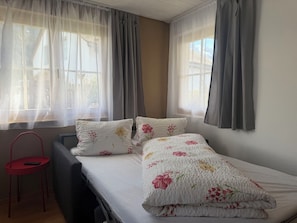 Ein Schlafzimmer mit einem Bett, zwei Kissen, einem Sessel und einem Fenster mit Vorhängen.