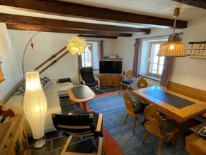 Ein gemütliches Wohnzimmer mit einer Couch, Sesseln, einem Esstisch und einem Fernseher.