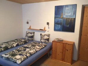 A single bed with patterned bedding, a wooden bedside table with a magazine, and a blue abstract painting on the wall. - Mugliner 117A, (Ftan) by Interhome (Ftan)