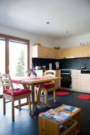 A modern kitchen with wooden cabinets, a dining table with chairs, and a view through a glass door. - Caviezel, (Tschlin) by Interhome (Tschlin)