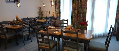 Un espace repas avec des tables et des chaises en bois, un coin café et une vue sur l’extérieur grâce à de grandes fenêtres.