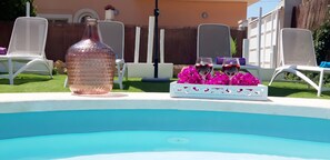Ein Pool mit weißem Rand, eine große Flasche und zwei Gläser mit rosa Blumen.