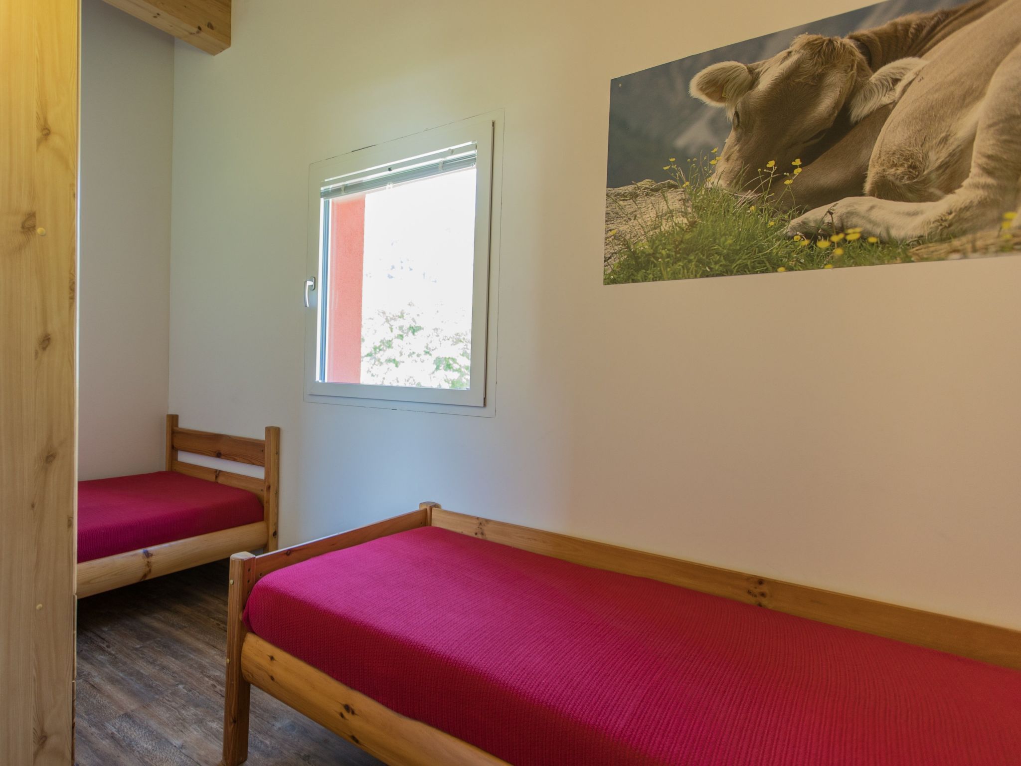 A room with two wooden beds, a window, and a wall-mounted picture.