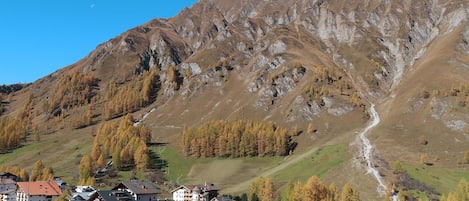 Un pueblo de montaña con edificios tradicionales, una carretera sinuosa y una imponente montaña al fondo.