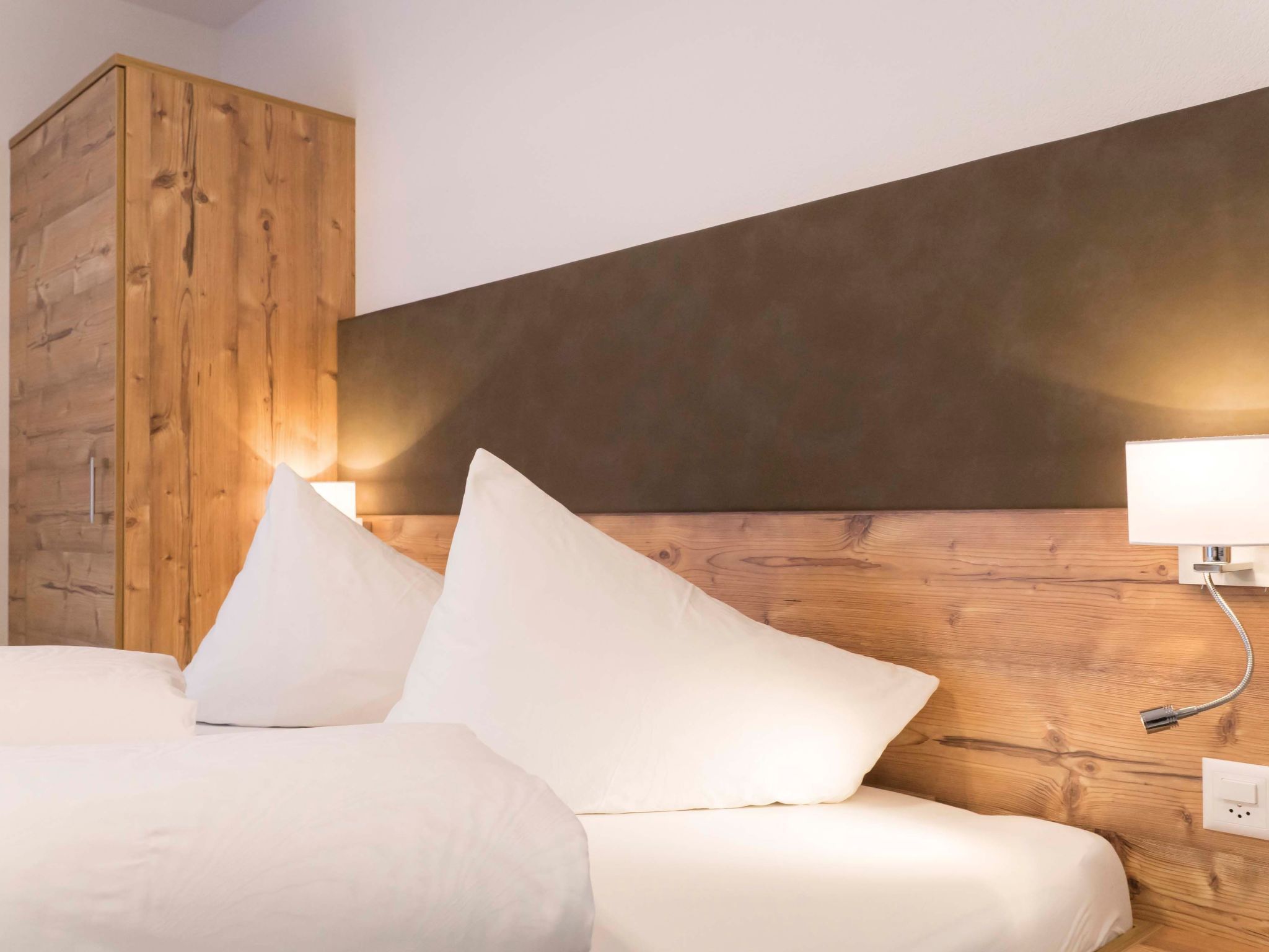 A bedroom with a wooden headboard, a bed with white bedding, and a nightstand with a lamp.