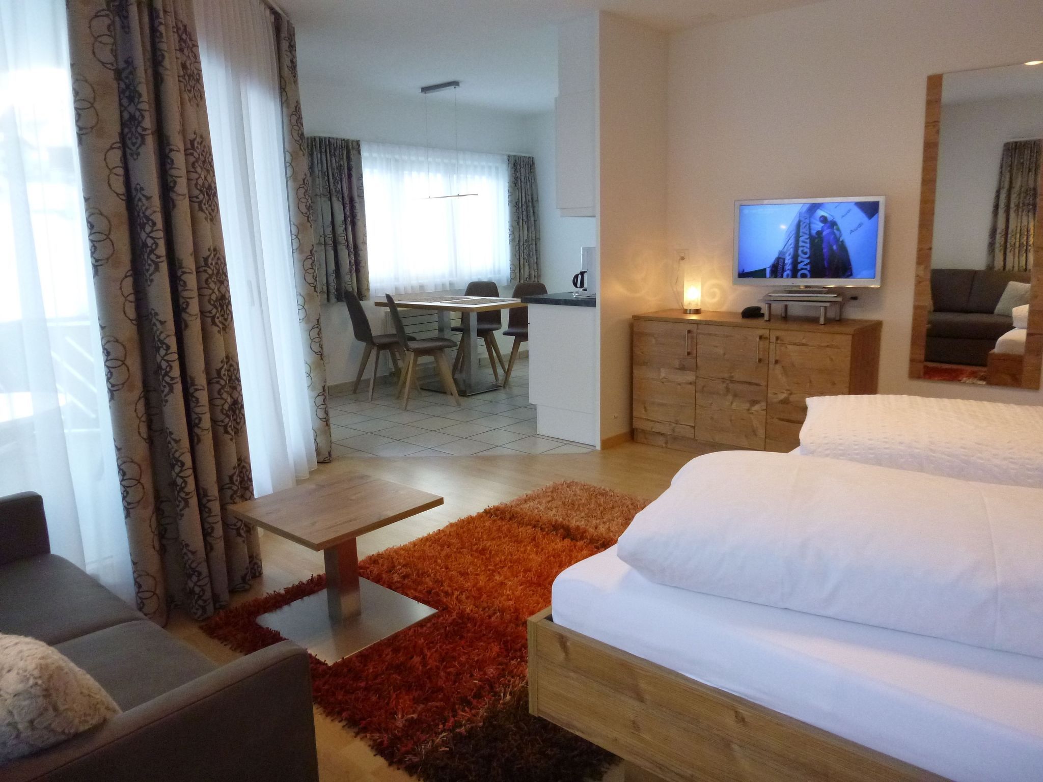 Une chambre d’hôtel avec un lit, un bureau, une télévision et, au fond, un coin repas.