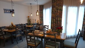 Et spiseområde med træborde og stole, en kaffestation og udsigt til det fri via store vinduer.