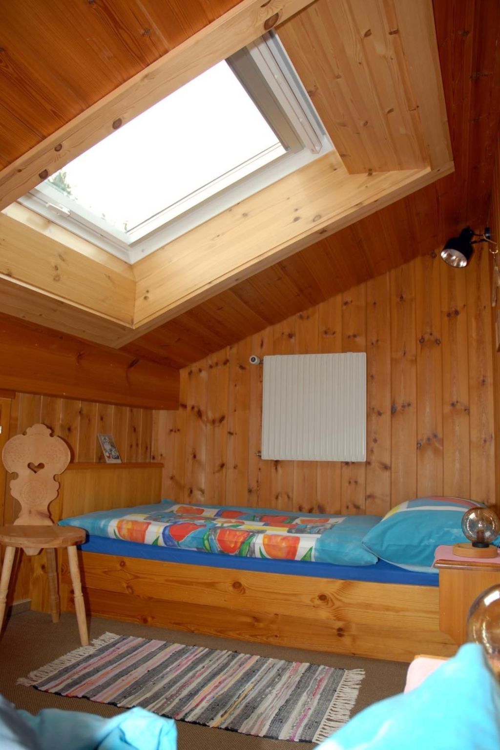 Een houten slaapkamer met dakraam, een bed met kleurrijk beddengoed, een houten stoel en een klein tafeltje met een wereldbol.