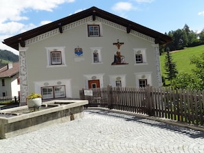 A building with a cross mural, a wooden fence, and a cobblestone courtyard. - Chasa Quadra, (Tarasp) by Interhome (Tarasp)
