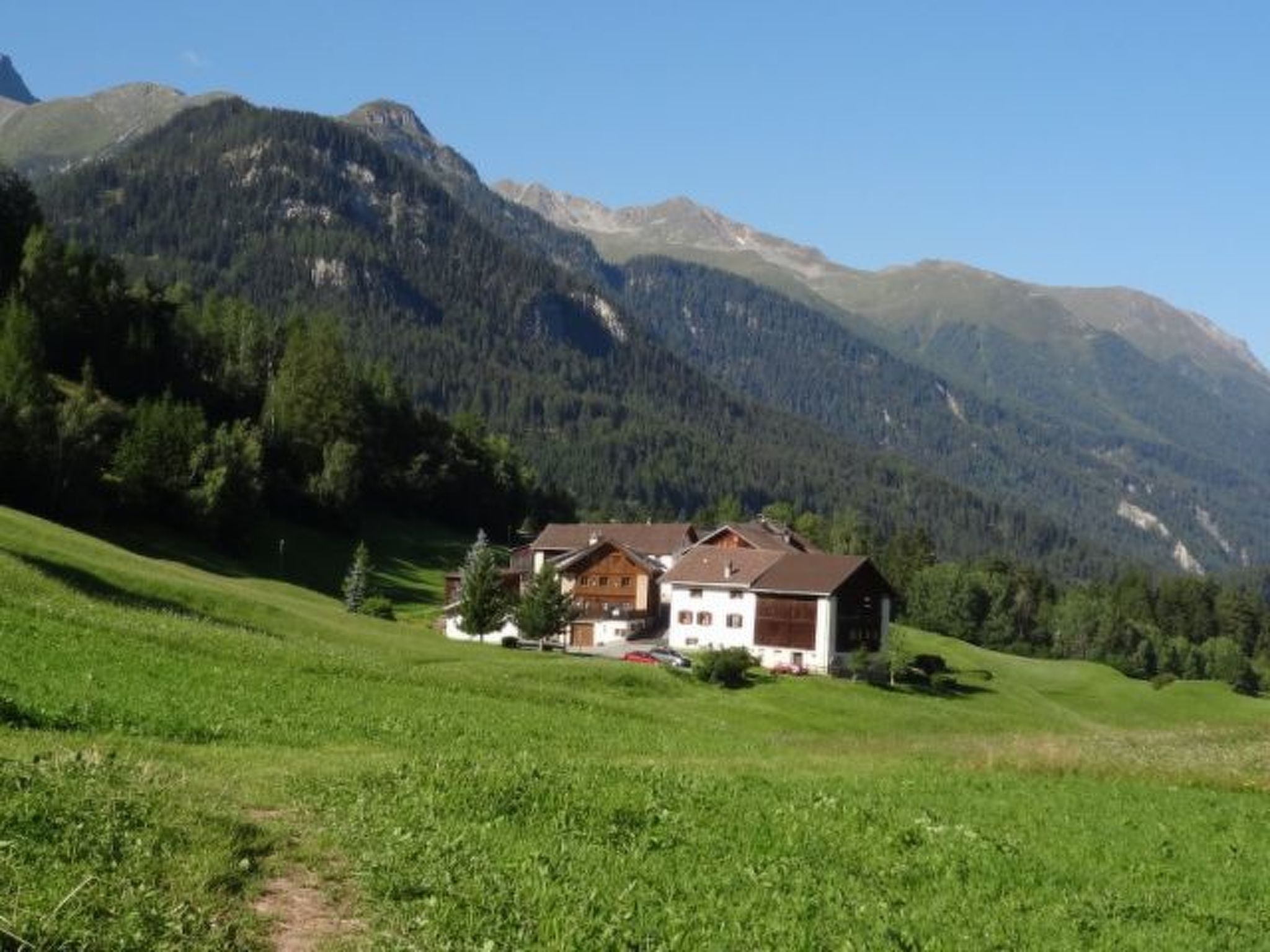Une maison avec un toit en pente, entourée d’un champ verdoyant et de montagnes.