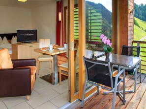 A modern room with a television, a dining table with chairs, a sofa, and a balcony with a view of green hills. - Apart Lischana, (Samnaun-Laret) by Interhome (Samnaun)