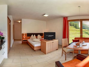 A hotel room with a bed, a TV, a dining table with chairs, and a view of greenery through the window. - Apart Lischana, (Samnaun-Laret) by Interhome (Samnaun)