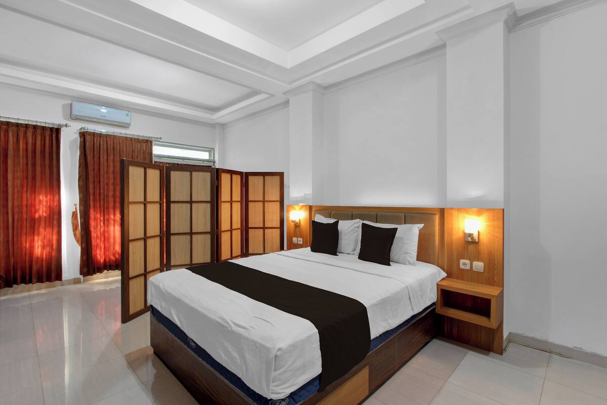 A modern hotel room with a large bed, wooden headboard, bedside tables, and a sliding shoji screen.