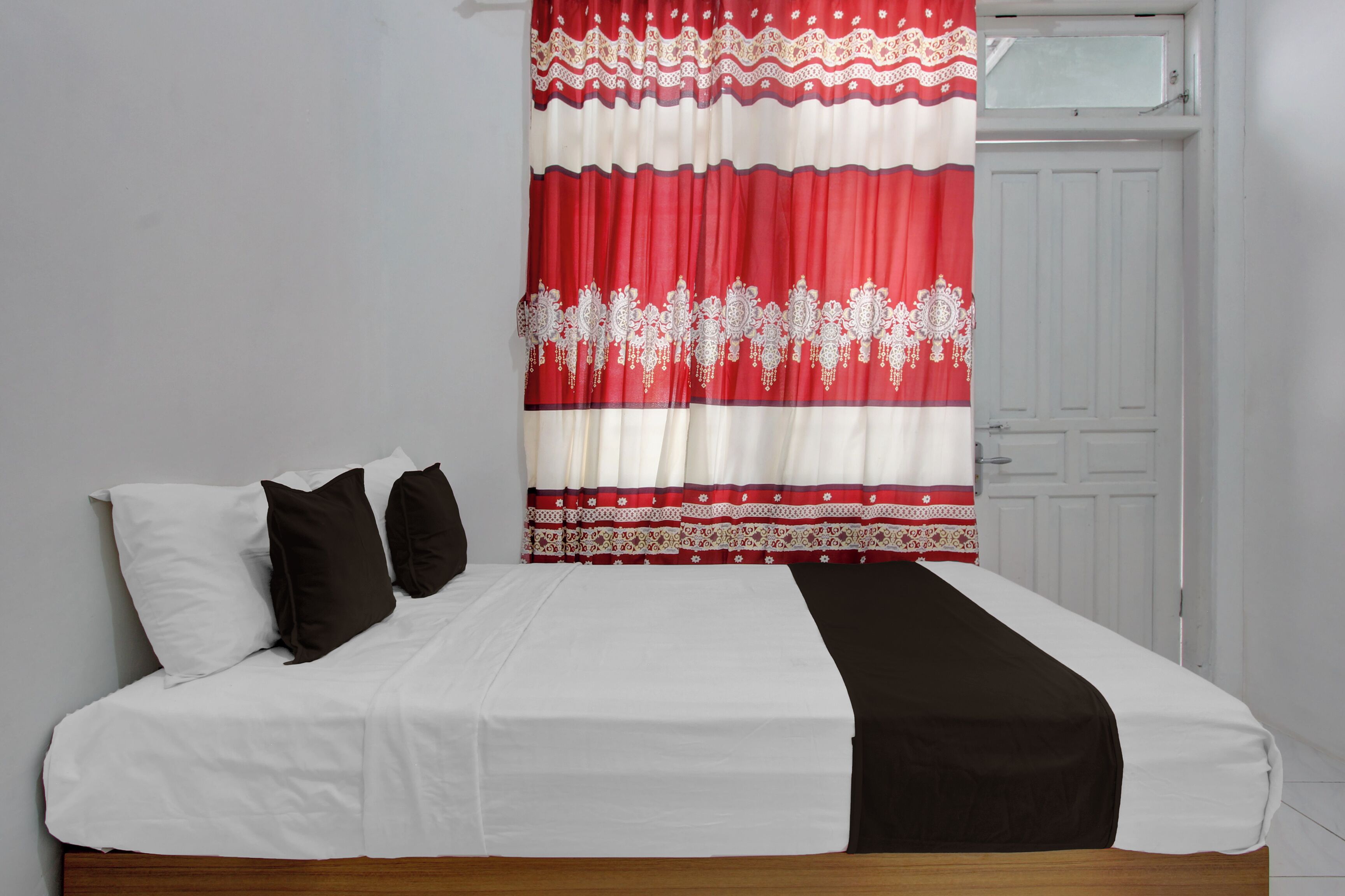A bed with white and black bedding, a red and white curtain, and a white door in the background.