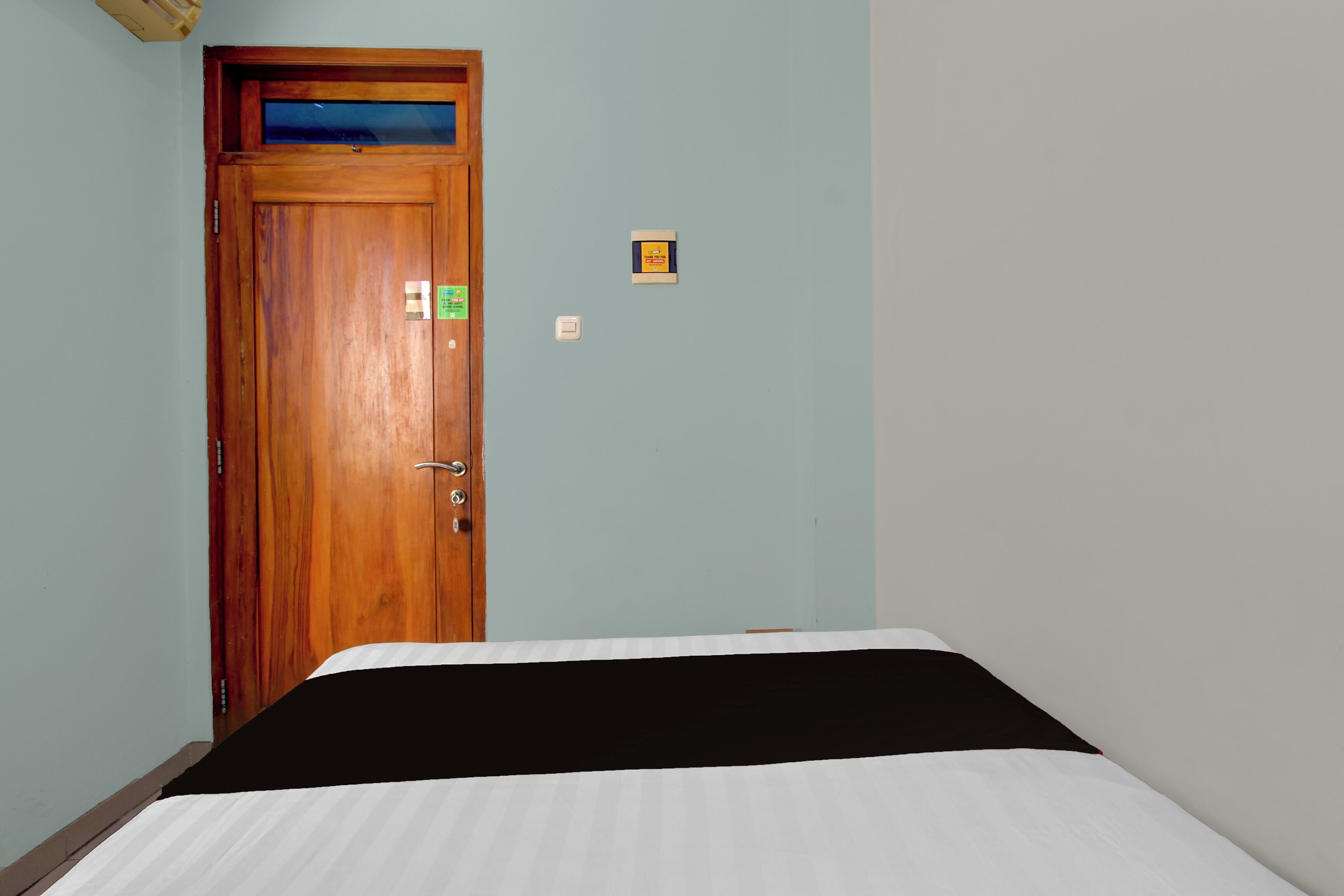 A room with a wooden door, a bed with a black and white bedspread, and a light blue wall.