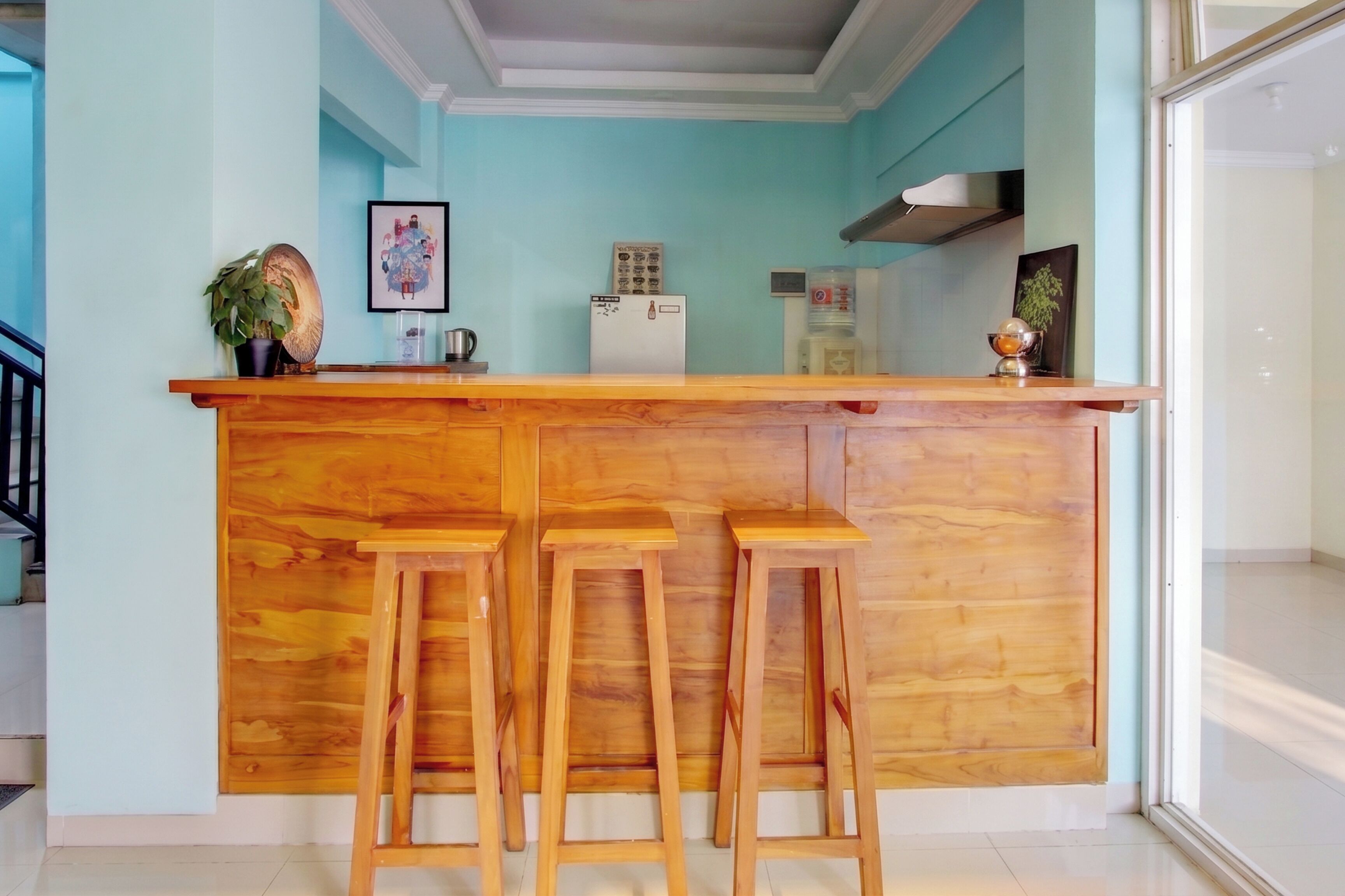 Une cuisine avec un bar en bois et des tabourets, un réfrigérateur et une plante.