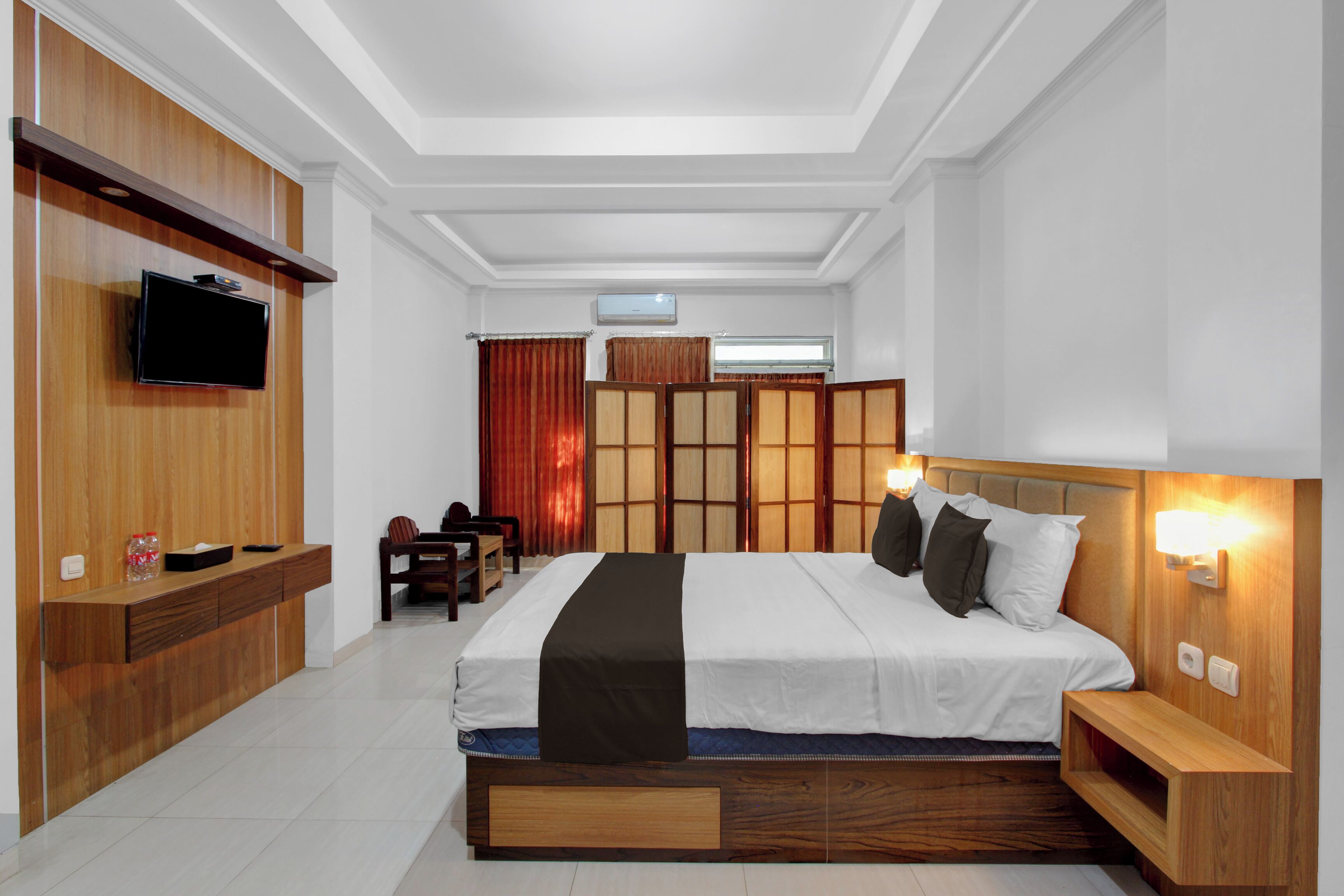 A modern hotel room with a large bed, wooden headboard, bedside tables, a flat-screen TV, and a built-in wardrobe.