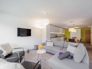 Ein modernes Wohnzimmer mit einem grauen Ecksofa, einem flachbildfernseher an der Wand und einem Essbereich mit Tisch und Stühlen.