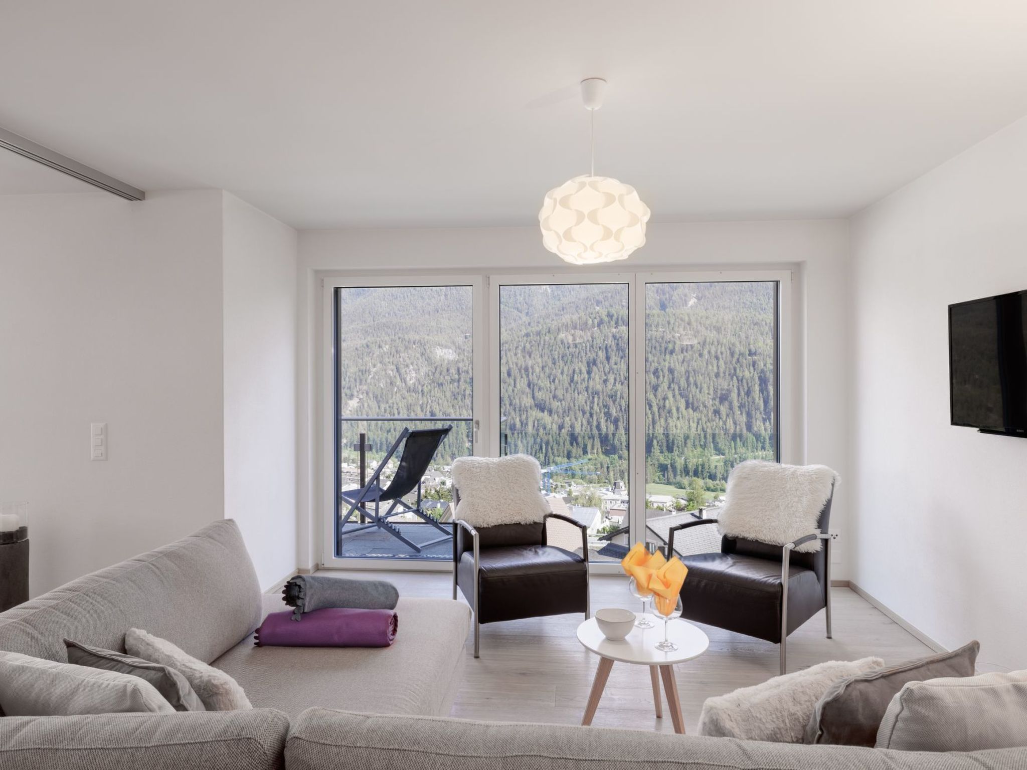 A modern living room with a sofa, two armchairs, a coffee table, and a large window offering a view of a forested area.