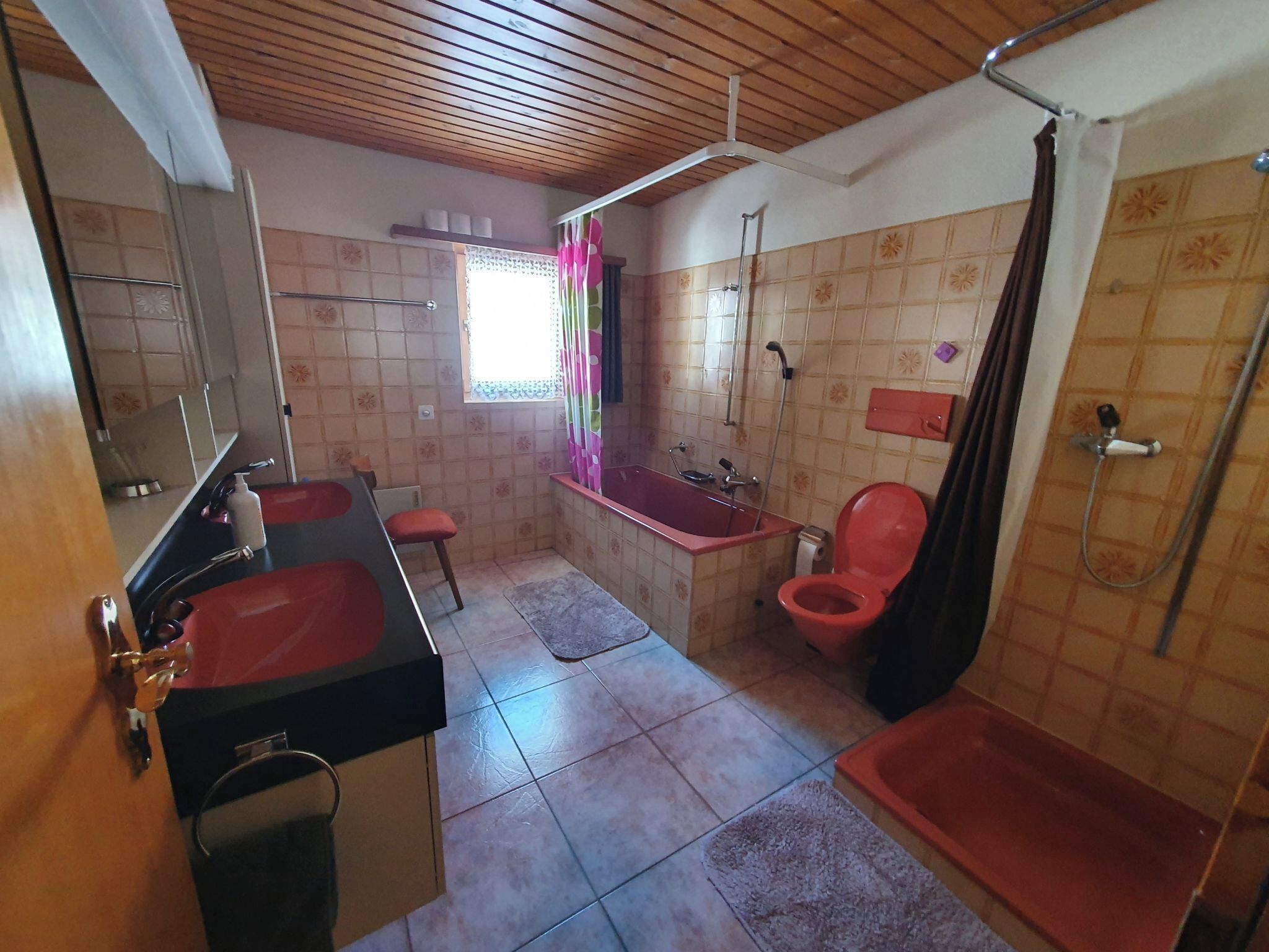 Ein Badezimmer mit Holzboden, einer roten Badewanne, einer Dusche, einer Toilette und einem Waschbecken.