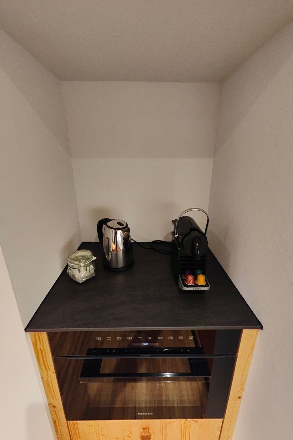 Uma cozinha compacta com cafeteira, chaleira e torradeira em bancada escura.