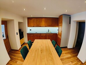 A modern kitchen with wooden cabinets, a central island, and a dining table with chairs. - Chasa Salnuun, (Samnaun-Compatsch) by Interhome (Samnaun)