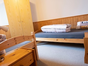 A single wooden bed with a mattress and pillows, a wooden chair, and a small wooden table with a lamp. - Archas 202A, (Sent) by Interhome (Sent)