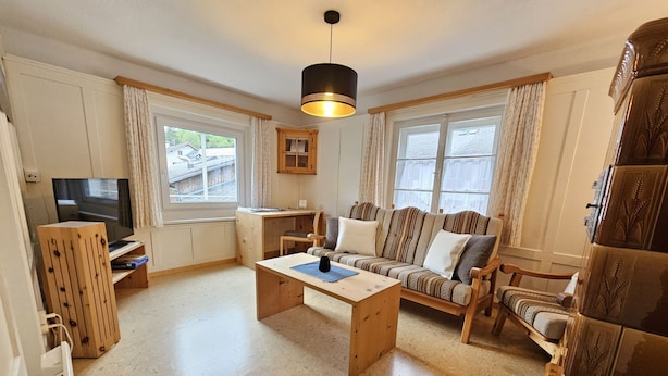 Een gezellige woonkamer met een houten bank, een salontafel, een televisie en een bureau.