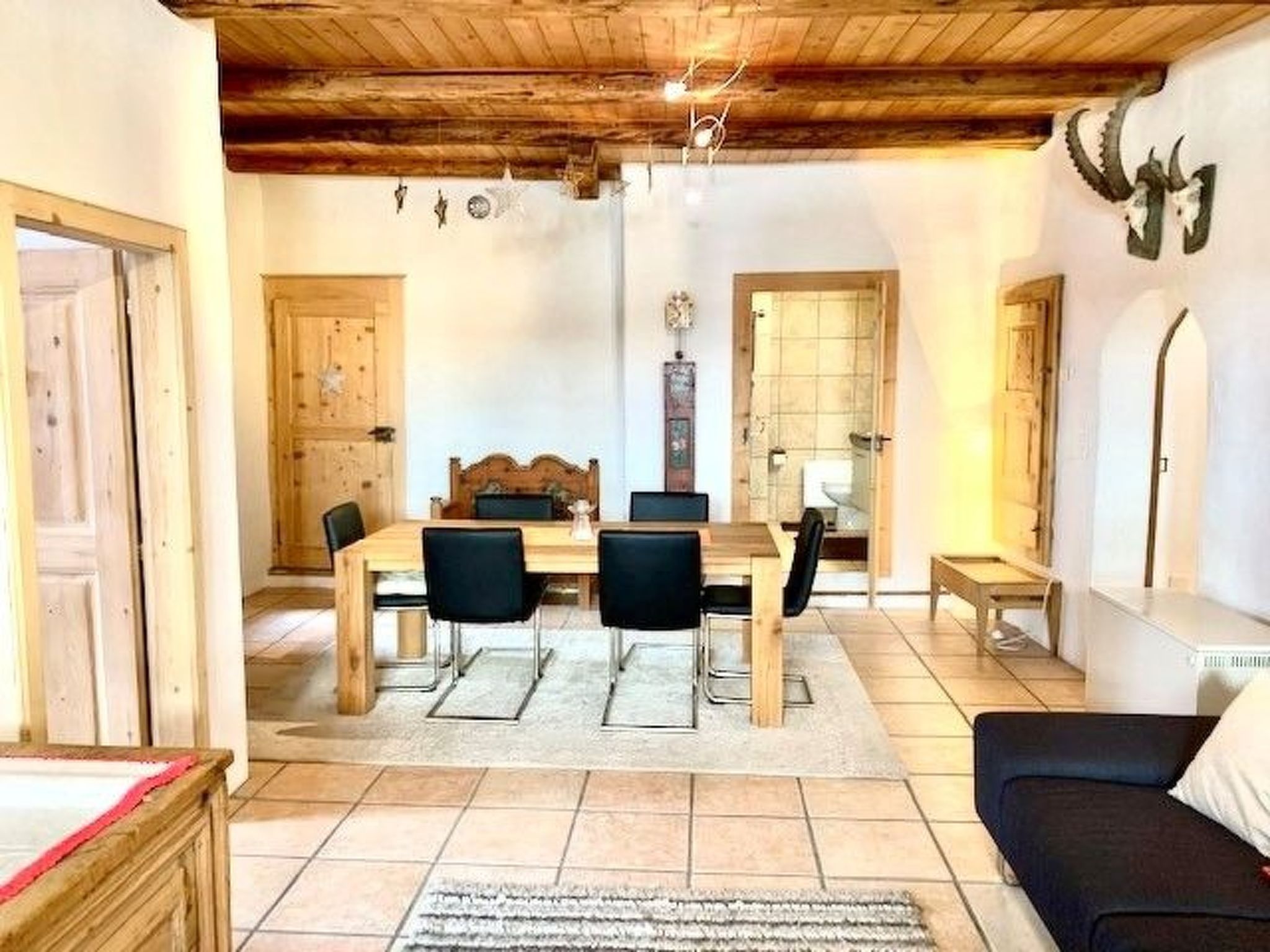 A dining area with a wooden table and chairs, a rug, and a ceiling with exposed beams.