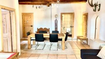 A dining area with a wooden table and chairs, a rug, and a ceiling with exposed beams.