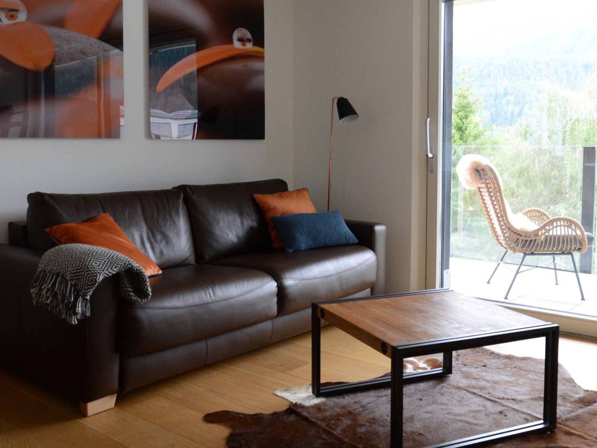 Un salon moderne avec un canapé en cuir, une table basse et une grande fenêtre donnant sur un paysage verdoyant.