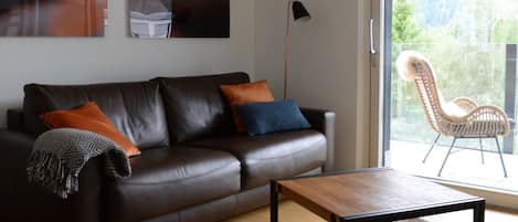 Un salon moderne avec un canapé en cuir, une table basse et une grande fenêtre donnant sur un paysage verdoyant.