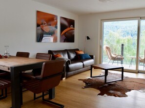 A modern living room with a dining table, leather sofa, and a large window with a view of a forest. - Chasa Rachögna, (Scuol) by Interhome (Scuol)