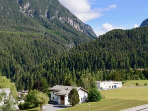A small building with a sloped roof, surrounded by a grassy area and a forested mountain backdrop. - Chasa Rachögna, (Scuol) by Interhome (Scuol)