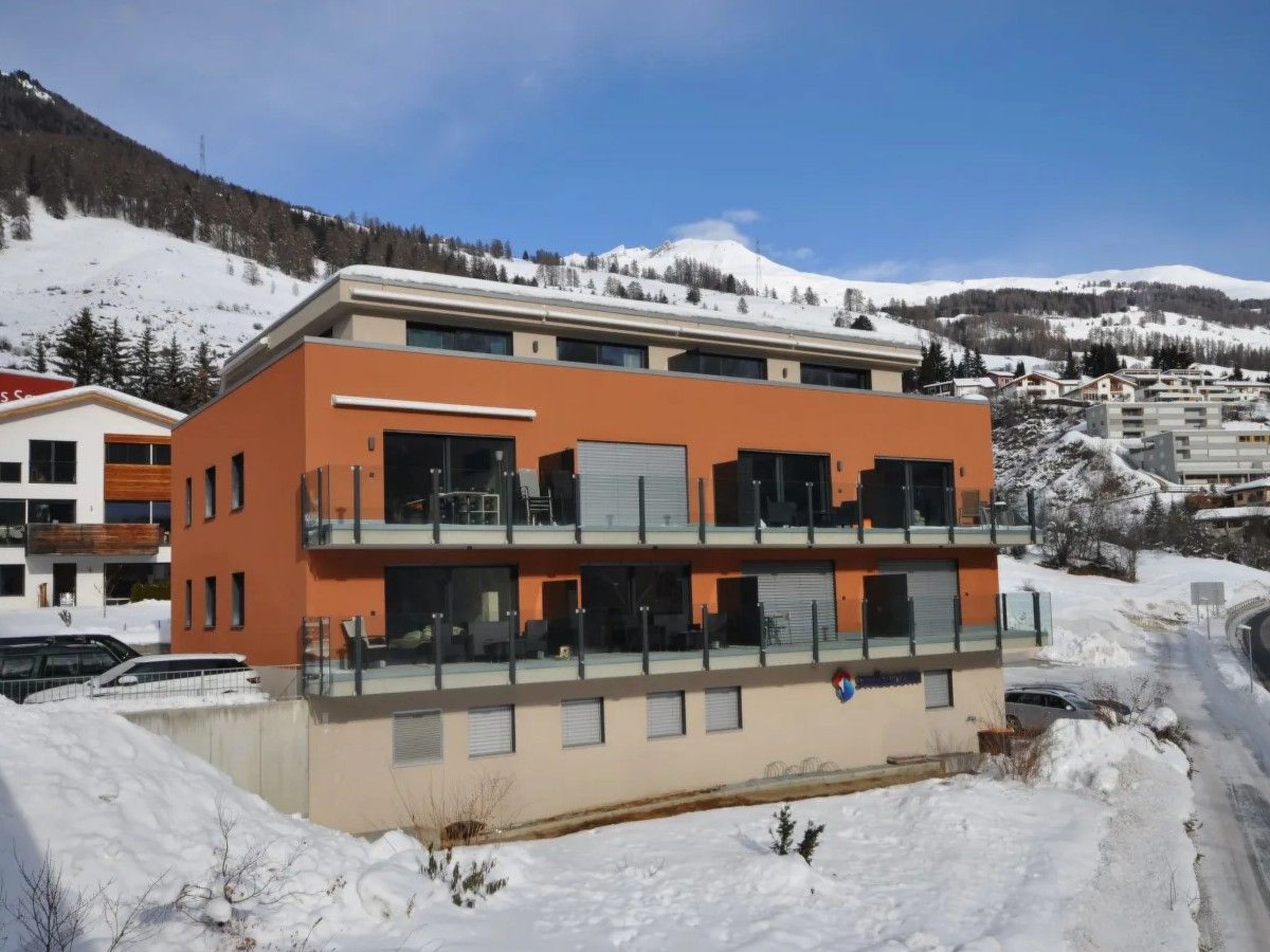 A modern two-story building with balconies, surrounded by snow-covered hills.