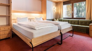 Une chambre d’hôtel avec deux lits, une tête de lit en bois, un canapé, une fenêtre avec des rideaux et une moquette rouge.