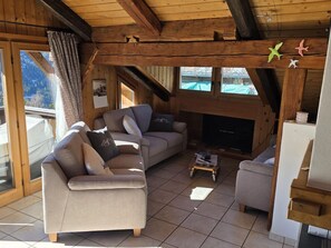 Una sala de estar acogedora con chimenea, vigas de madera y un ventanal con vistas a un paisaje montañoso.